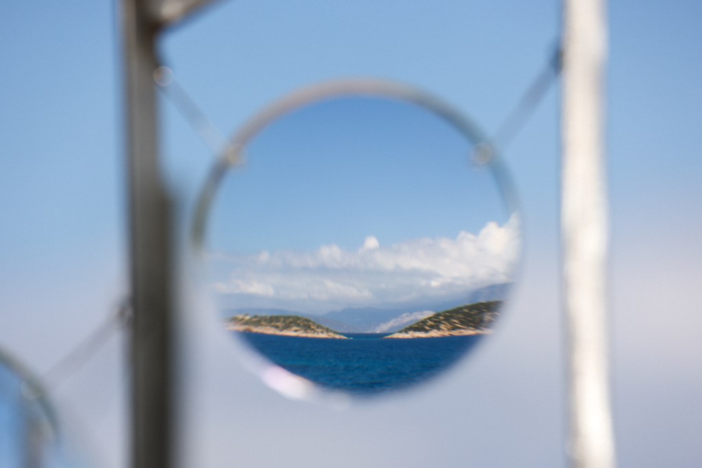 A scenic view of an island and the ocean reflected in a circular lens, with a clear blue sky and clouds in the background.